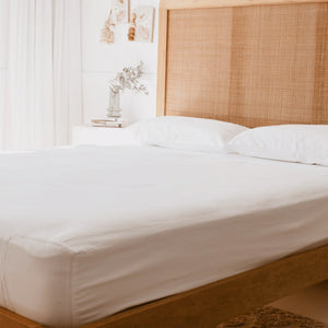 queen bed with rattan had board and white curtains with white pillowcases and white fitted sheet, showing the corner of the fitted sheet has an additional stretch panel
