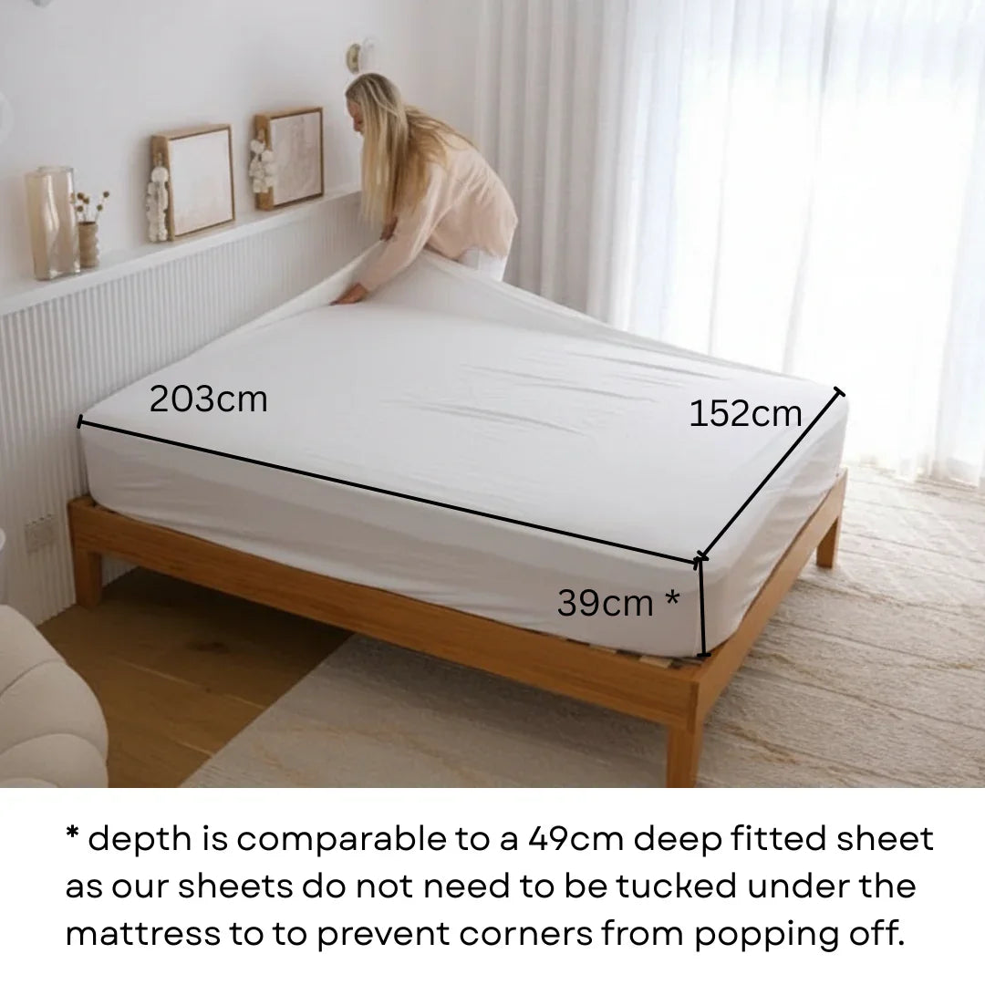 Person measuring a mattress with dimensions displayed on a bed in a bedroom on a Arthritis-friendly fitted sheet corner design
