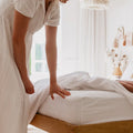 Female looking at corner of white fitted sheet after pullin back the covers on the queen bed