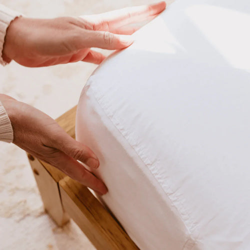 Female hands touching the corner of a white fitted sheet on a queen bed, can only see the corner of the bed